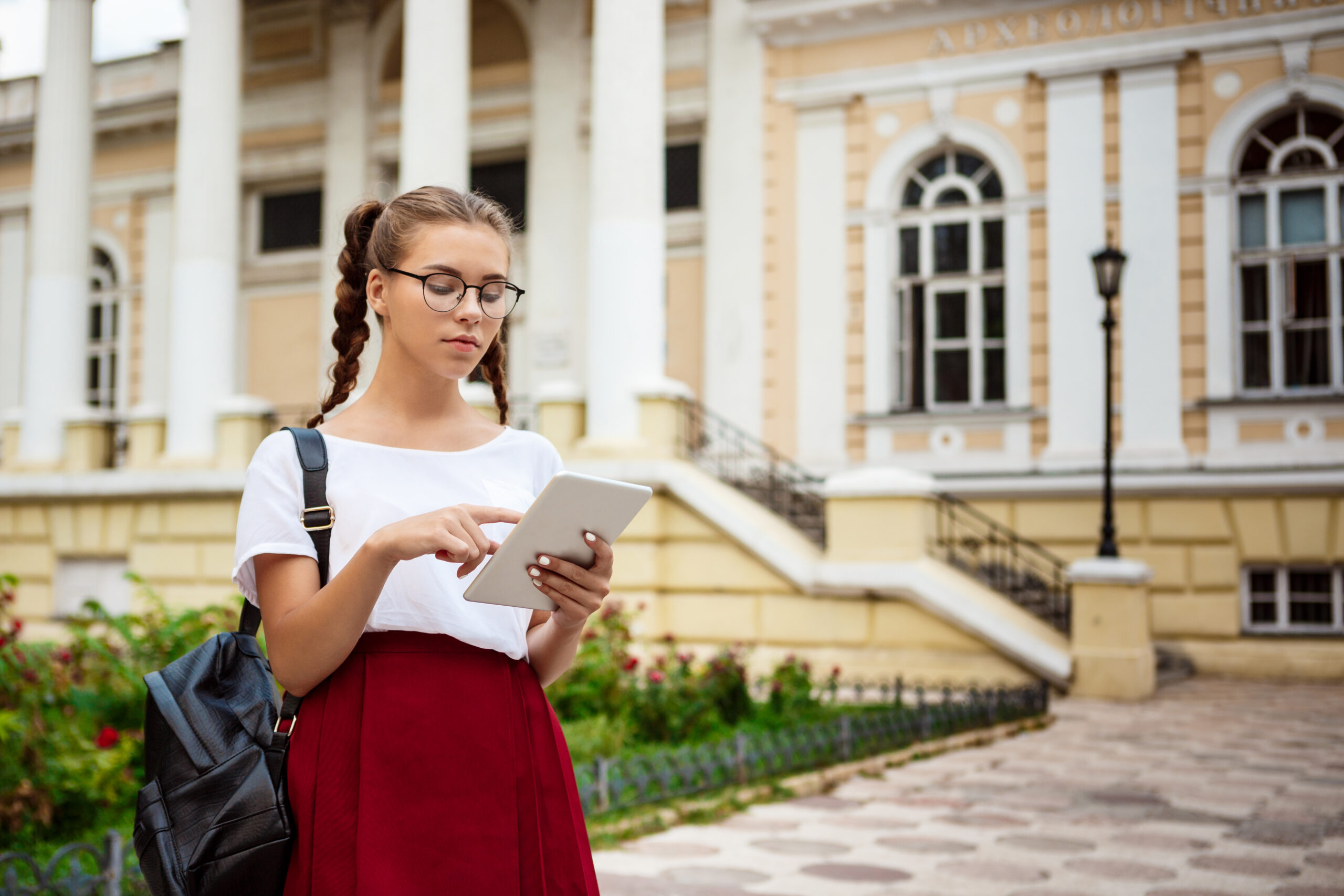 Young beautiful female student looking at tablet outdoors, park background.